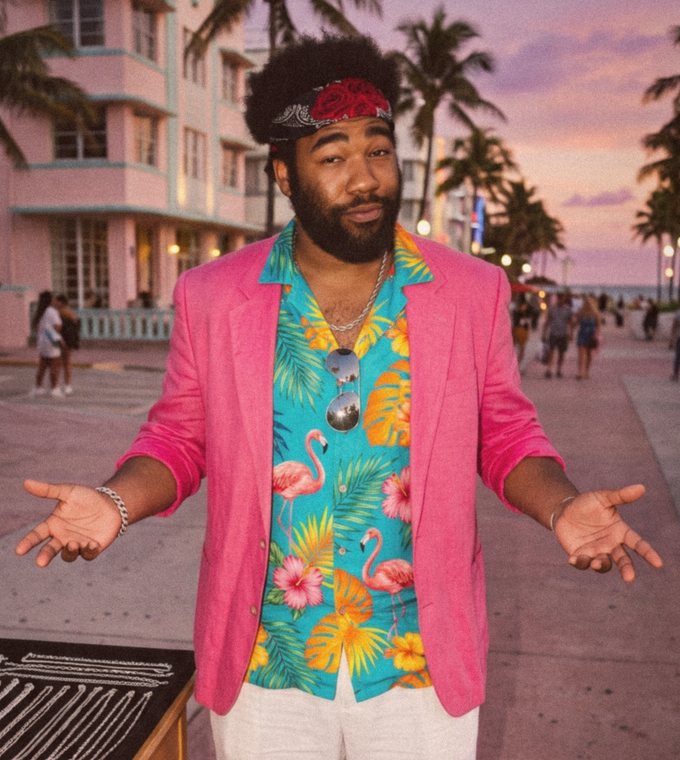 Sonny Silva shrugging with both palms up, one eyebrow raised, on the boardwalk at sunset