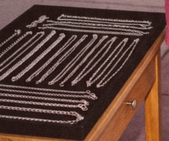 Rows of silver chains laid out on the black velvet tray of a wooden cart
